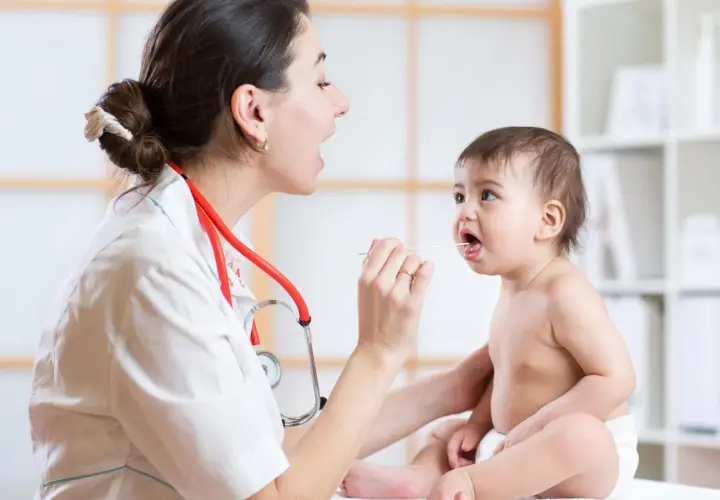 Medico esamina la gola di un bambino con abbassalingua, controllando sintomi di laringite bambini.