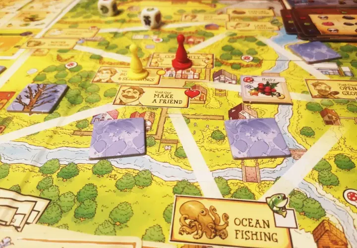 Planszowa gra Stardew Valley z pionkami, kostkami i kartami postaci. Na planszy widać rzekę, domy i pola.