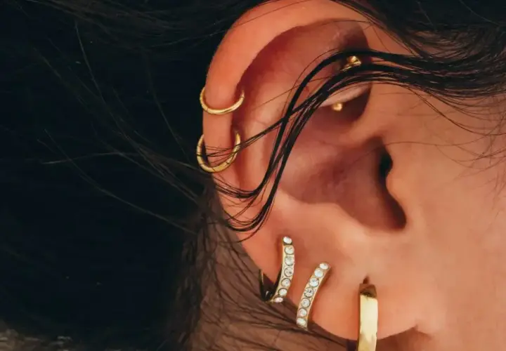 Ucho ozdobione złotymi kolczykami, w tym subtelnym conch piercingiem, podkreśla indywidualny styl.