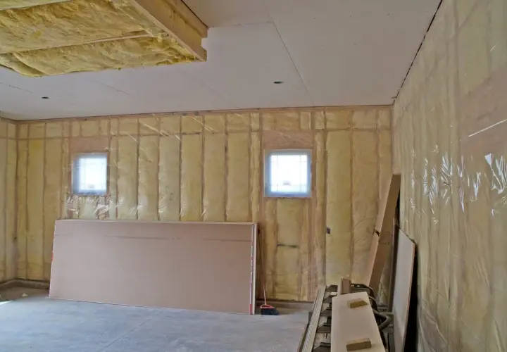Travaux en cours pour isoler un garage non chauffé. Isolation jaune visible sur les murs et le plafond, avec des plaques de plâtre et des fenêtres.