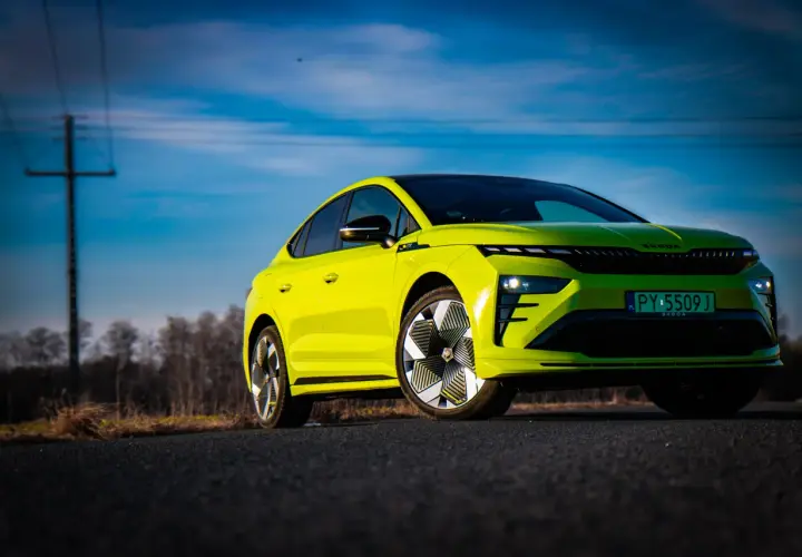 Jaskrawozielony Skoda Enyaq Coupe na tle błękitnego nieba z chmurami i linią energetyczną.