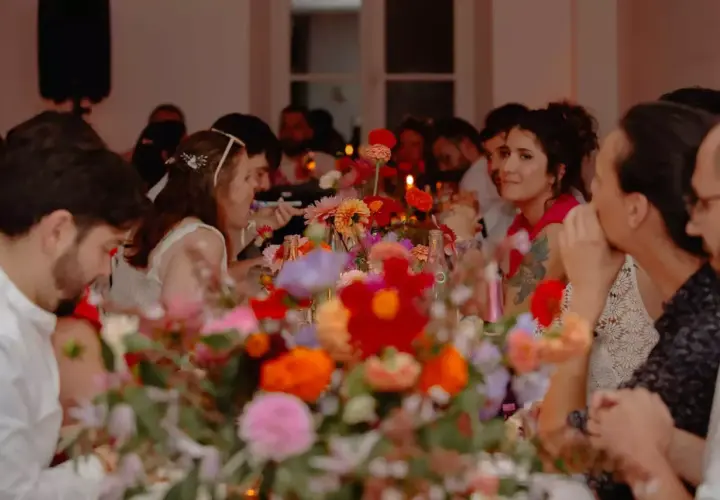 Des invités souriants partagent un repas de mariage festif, entourés de fleurs colorées. La durée du repas semble agréable.