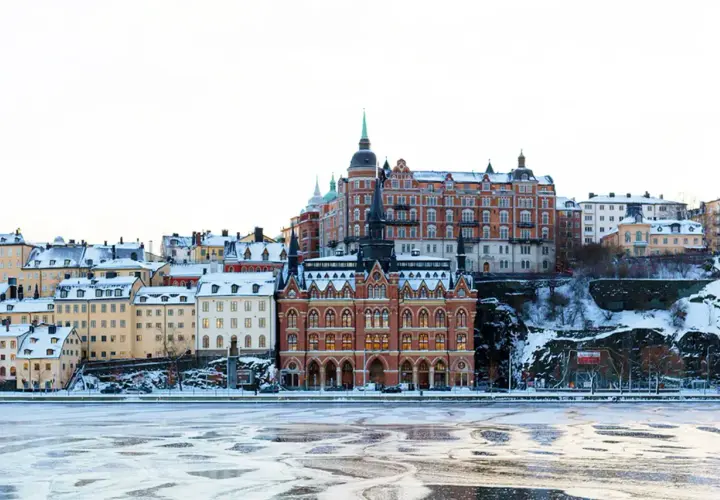Vinter i Stockholm: snöklädda hus längs vattnet, perfekt för mysiga promenader och fika.