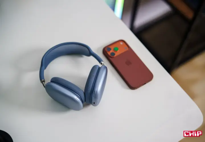 Niebieskie słuchawki AirPods Max i brązowy iPhone na białym biurku. Dowiedz się, jak połączyć AirPods z PC.