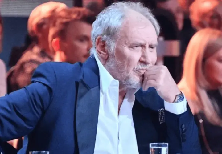 Andrzej Grabowski żyje, siedzi w eleganckim garniturze, zamyślony, z dłonią przy ustach. W tle widać innych ludzi.