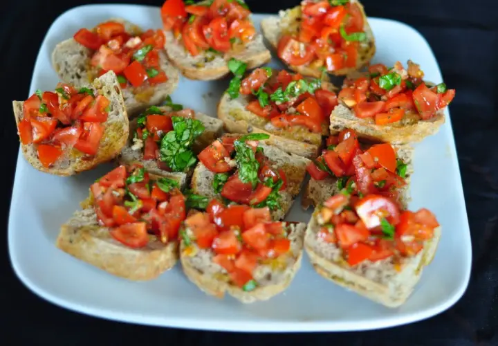 Bruschetta z pomidorami i bazylią, ułożona na białym talerzu. Chrupiące grzanki z dodatkiem świeżych, soczystych pomidorów i aromatycznej bazylii.