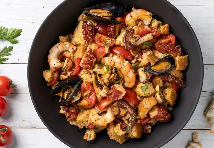Panzanella di mare ricca con gamberi, polpo, cozze e pomodori, condita con pane raffermo. Un piatto estivo saporito.
