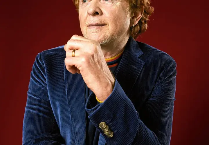 Mężczyzna z rudymi włosami, w granatowej sztruksowej marynarce, z dłonią na brodzie. To wokalista Simply Red.