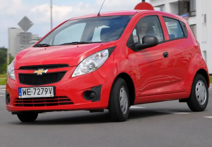 Czerwony Chevrolet Spark na drodze. Kierowca w środku. Wiele osób szuka chevrolet spark opinie przed zakupem.