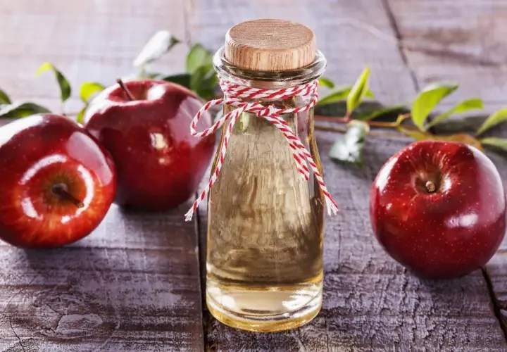 Rote Äpfel und eine Flasche Apfelessig auf Holz. Die natürliche Apfelessig Wirkung auf die Haut ist ein Geheimnis der Schönheit.