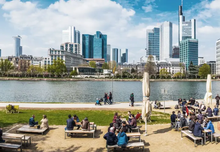 Frankfurt Geheimtipps: Menschen genießen das Leben am Mainufer mit Blick auf die Skyline. Ein perfekter Ort zum Entspannen und Beobachten.