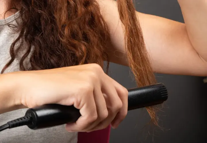 Ruda kobieta uczy się, jak zakręcić loki prostownicą, tworząc piękne fale na swoich długich włosach.