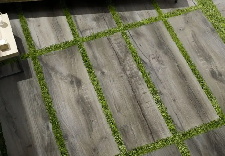Pavimento posa a secco su erba, con doghe effetto legno grigio alternate a strisce di prato verde. Un tavolino da caffè completa la scena.