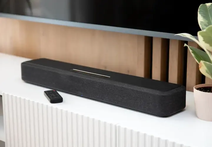Czarny soundbar z pilotem na białej komodzie, element zestawienia najlepszych soundbarów.