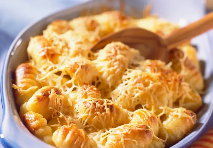Un plat de gratin de gnocchi doré et gratiné au fromage, prêt à être servi avec une cuillère en bois.