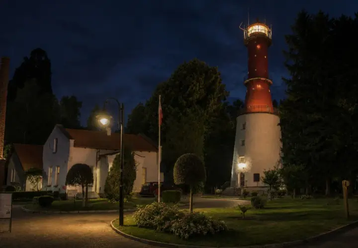 Nocna panorama latarni morskiej Rozewie. W oddali widać charakterystyczną czerwoną wieżę, a bliżej białe budynki i ceglany komin.