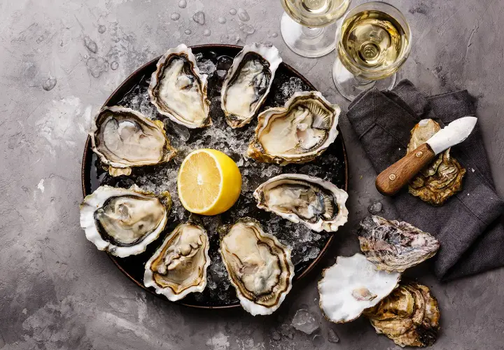Plateau d'huîtres fraîches avec citron, deux verres de vin blanc, parfait pour le meilleur vin blanc pour fruits de mer.