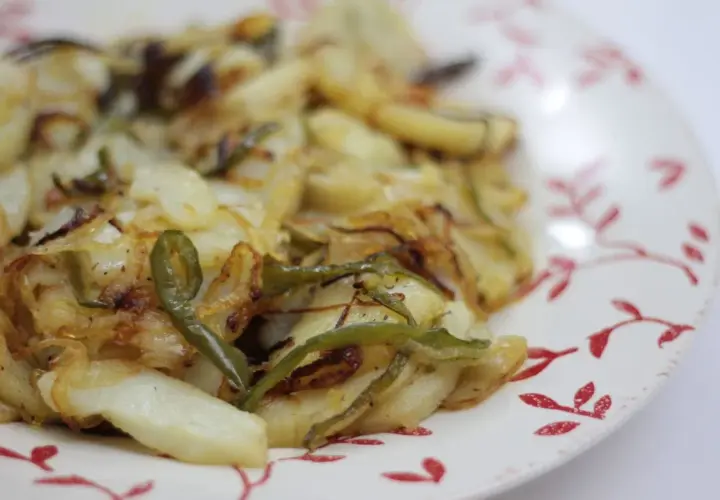 Plato de patatas panaderas al horno con cebolla y pimientos verdes, recién sacadas del horno y listas para disfrutar.