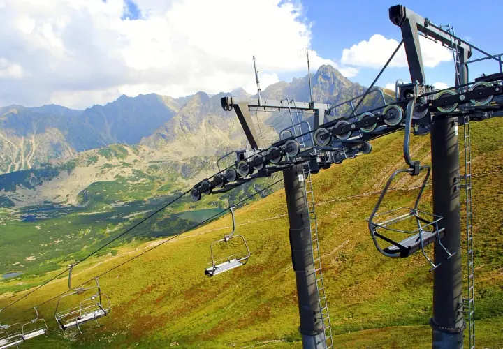Wyciąg krzesełkowy Zakopane wita w Tatrach. Puste krzesełka wiszą na tle gór i zielonych zboczy.