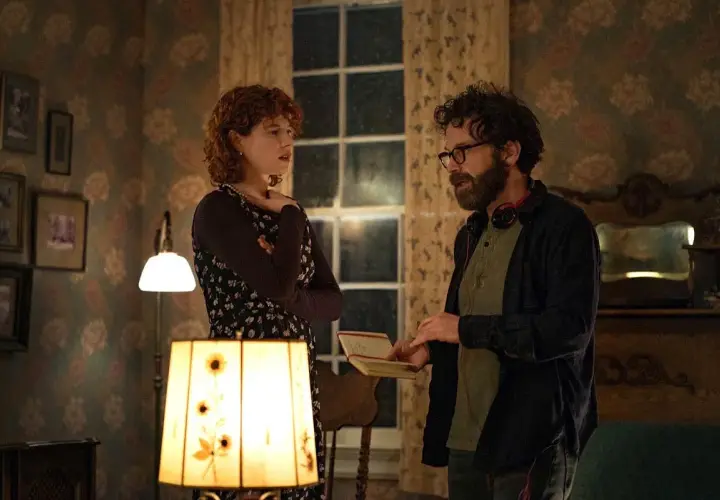 Una donna con capelli rossi e un uomo con occhiali discutono animatamente in una stanza. Lui tiene un quaderno, forse sto pensando di finirla qui recensioni.