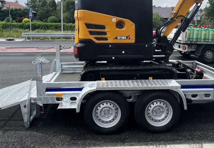Żółta mini koparka SY18C na przyczepie z rampą. Waga maszyny pozwala na łatwy transport.