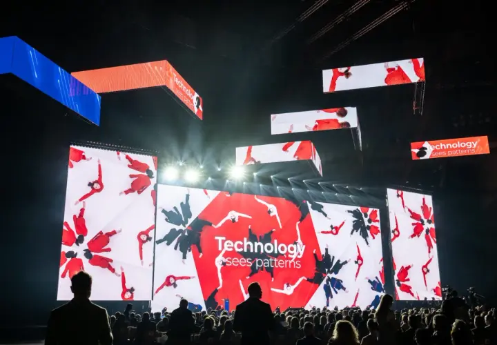 Wielkie ekrany na scenie pokazują ludzi w czerwonych strojach, tworzących wzory. To inspiracja, jak zarabiać na zdjęciach, wykorzystując kreatywność i technologię.