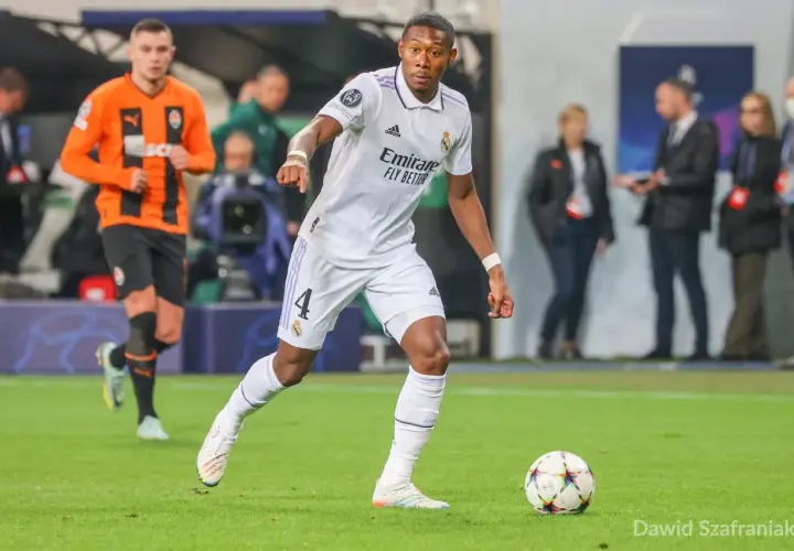 Piłkarz Realu Madryt w białej koszulce z numerem 4, David Alaba, prowadzi piłkę. W tle widać zawodnika Szachtara Donieck w pomarańczowej koszulce. To obraz jednego z najlepszych obrońców świata.