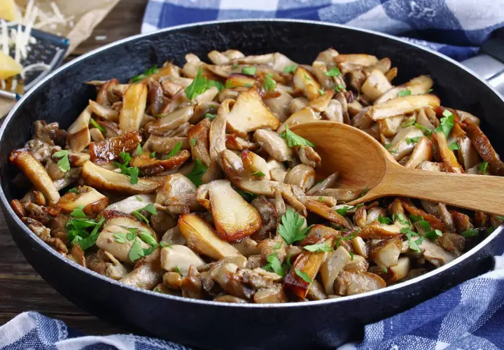 Une poêle débordante de fondue savoyarde aux cèpes, garnie de persil frais. Une cuillère en bois repose sur ce délice forestier.