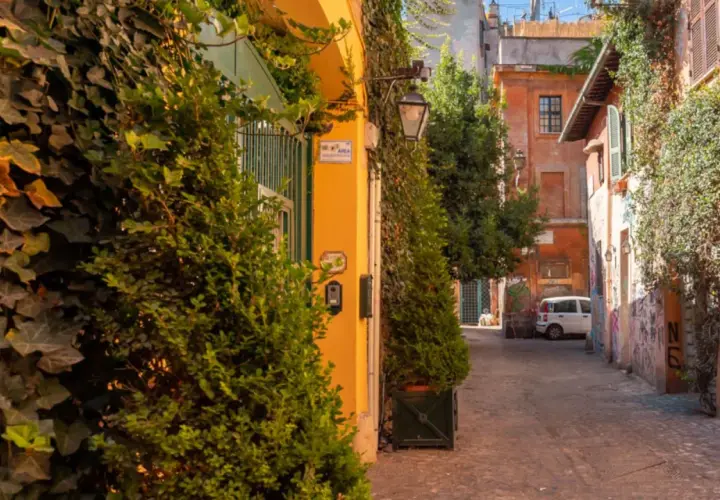 Un vicolo pittoresco tra le vie di Roma centro, con edera rampicante, edifici colorati e un'auto bianca parcheggiata.