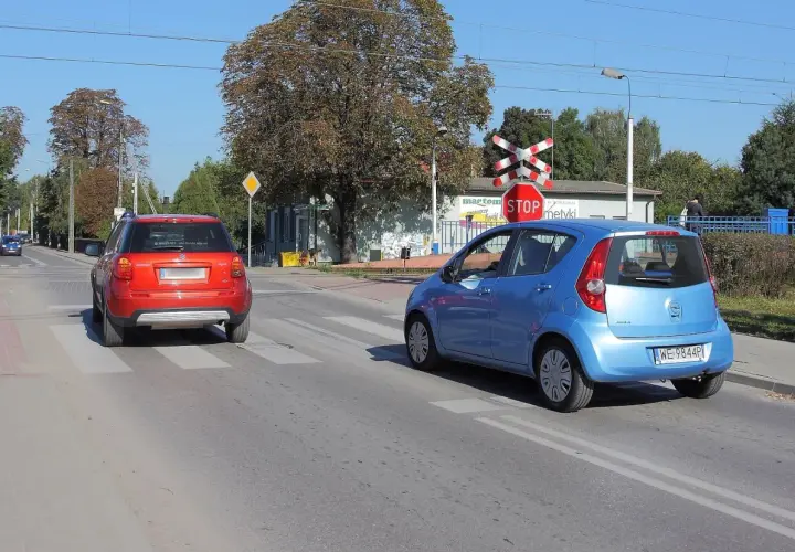 Czerwony i niebieski samochód na przejściu dla pieszych, czerwony czeka na wymijanie, niebieski już rusza.