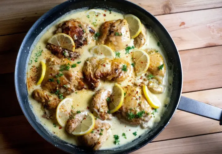 Succulento petto di pollo al limone in padella, guarnito con fette di limone fresco e prezzemolo tritato.
