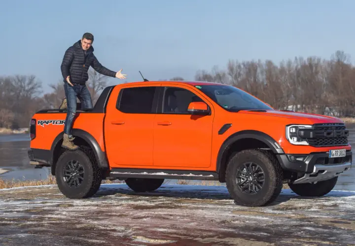 Pomarańczowy Ford Ranger Raptor z kierowcą na pace, gotowy na zimową przygodę nad rzeką.