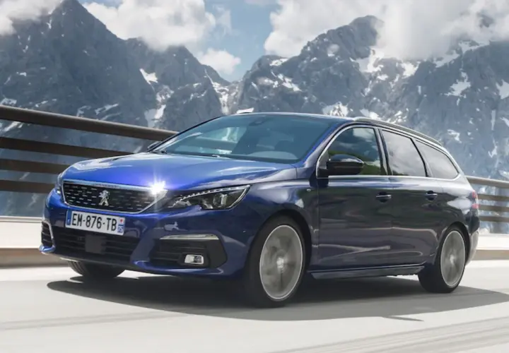 Niebieski Peugeot 308 T9 kombi jedzie po górskiej drodze, z ośnieżonymi szczytami w tle.