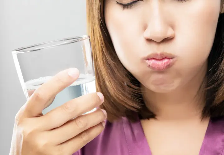 Frau mit geschlossenen Augen hält ein Glas Wasser und spült sich den Mund aus. Ein erfrischendes salzwasser am morgen Ritual.