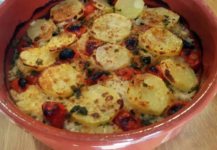 Piatto di riso patate e cozze cotto al forno, con pomodorini e erbe aromatiche, servito in una terrina di terracotta.