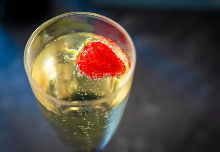 Une fraise flotte dans un verre de soupe angevine pétillante, créant une image rafraîchissante.