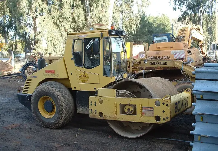 Żółty walec drogowy BOMAG BW 213D-3, obok koparka Samsung Caterpillar. Szerokość koparki nie jest widoczna, ale walec jest imponujący.