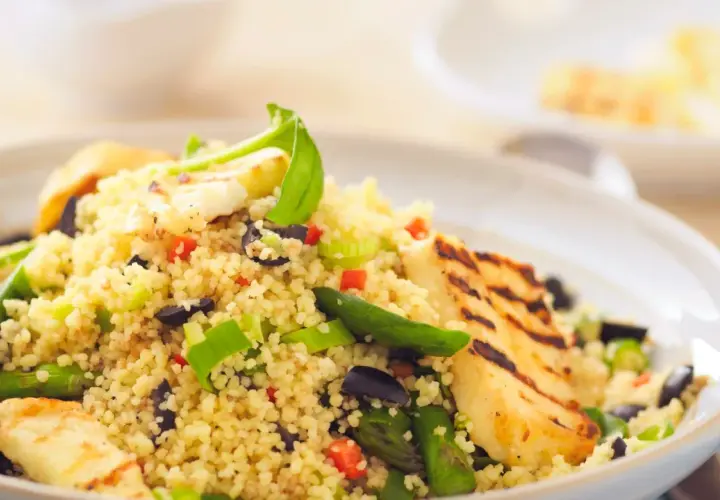Un piatto colorato di cous cous con verdure miste, olive nere e cubetti di formaggio grigliato.