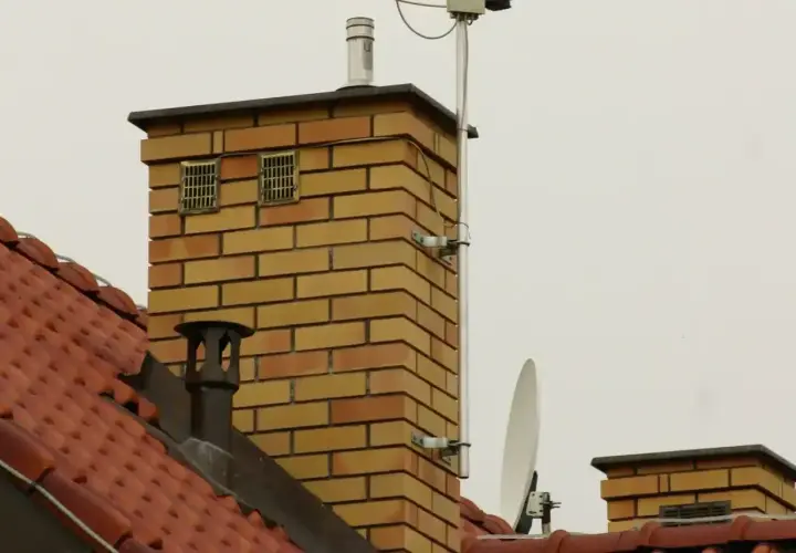 Ceglanego komina z dwoma kratkami wentylacyjnymi, które mogą służyć jako odpowietrzenie kanalizacji. Na dachu widać antenę satelitarną.