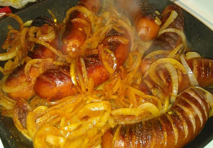Gorąca kiełbasa z cebulą skwierczy na patelni, tworząc apetyczny aromat.