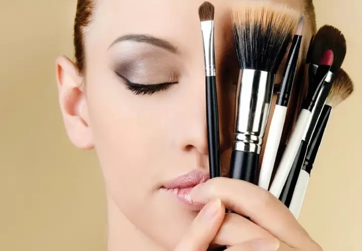 Mujer con ojos cerrados y varios pinceles de maquillaje, inspirando ideas de maquillaje.