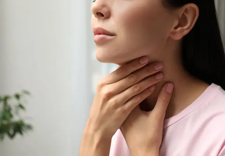 Kobieta dotyka szyi, być może odczuwając dyskomfort związany z tarczycą, który może być leczony np. thyrozolem.
