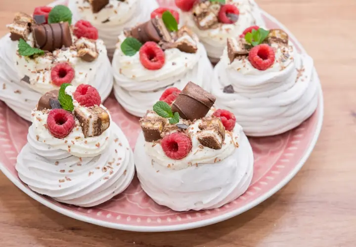 Słodkie mini pavlova z bitą śmietaną, malinami i kawałkami czekolady na różowym talerzu.