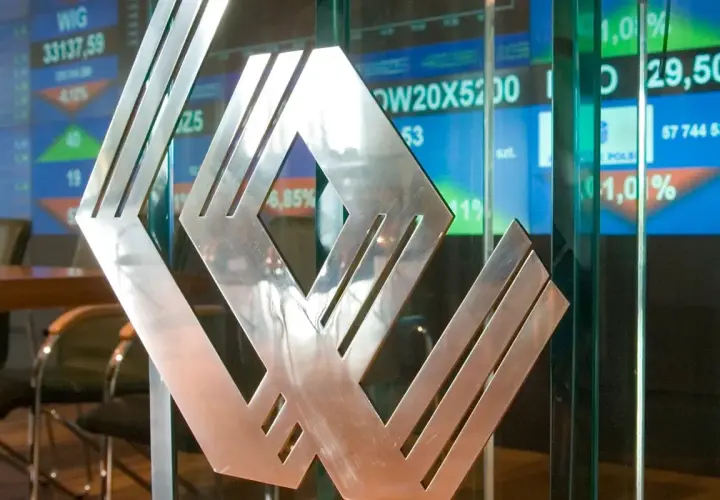 Metalowe logo na tle ekranów giełdowych. Asbis rekomendacje widać na wykresach.