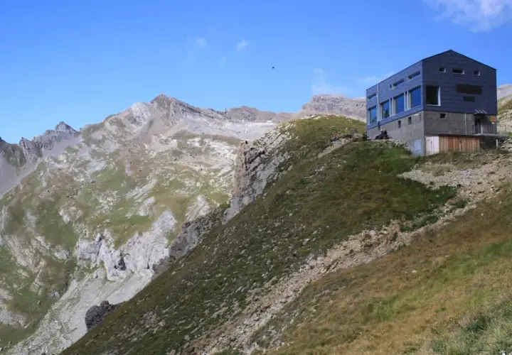 Moderne Hütte am Hang, Teil der Tour des Muverans, mit steilen Felswänden und grünen Bergwiesen im Hintergrund.