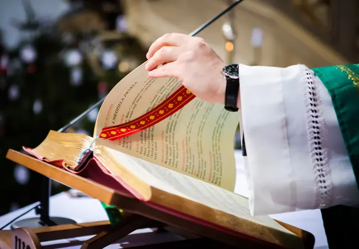 Dłoń księdza przewracająca kartki księgi liturgicznej na pulpicie.