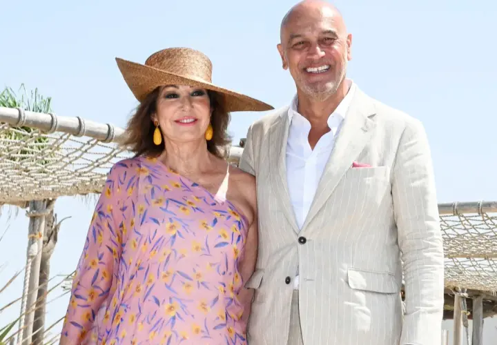 Ana Rosa Quintana y su marido celebran la boda de su hijo. Ella luce un vestido floral y sombrero, él un traje claro.