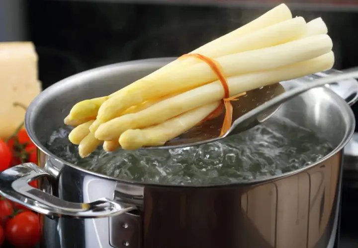 Un bouquet d'asperges blanches est plongé dans l'eau bouillante pour une cuisson parfaite.