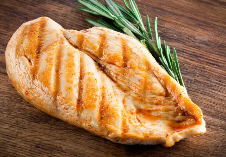 Grillowana pierś kurczaka z rozmarynem na drewnianej desce. Pytanie: ile białka ma kurczak?