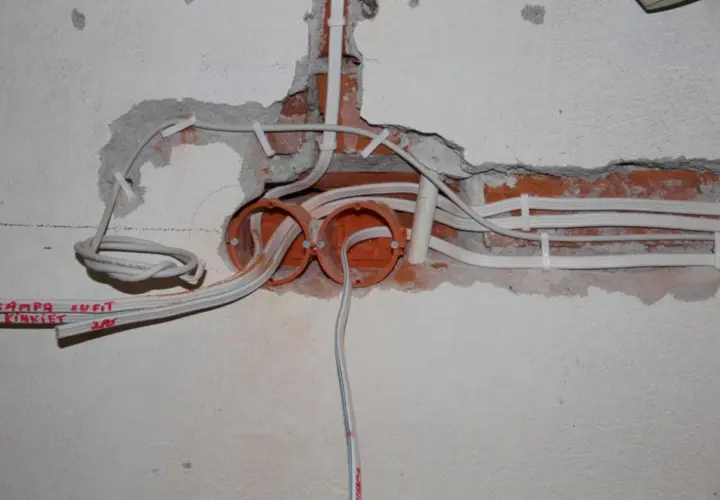 Rozpoczęta wymiana instalacji elektrycznej: widoczne puszki, przewody i fragmenty ceglanej ściany.